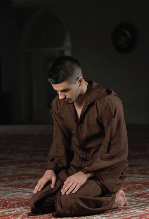 Young Muslim man sitting in prayer position inside a mosque